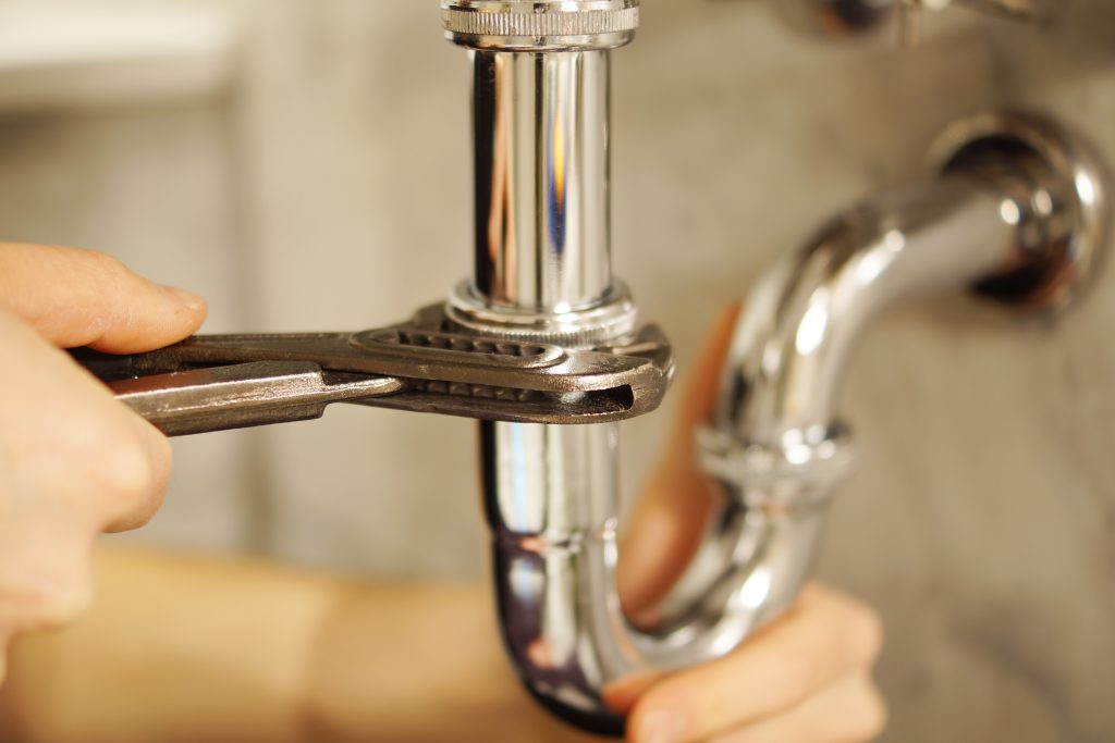Plumbing repair service. Professional installer with spanner checking pipe
