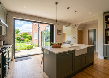 Modern kitchen with green cabinets, central island, garden view through open doors, wooden floor, stylish decor
