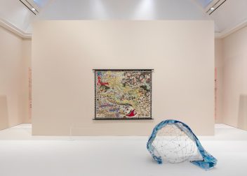 Contemporary art installation with a colourful map tapestry and a blue-accented sculpture in a minimalist gallery setting