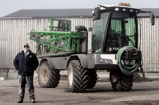 Farmer standing proudly beside a large agricultural tractor at a farmyard, showcasing farming equipment and machinery