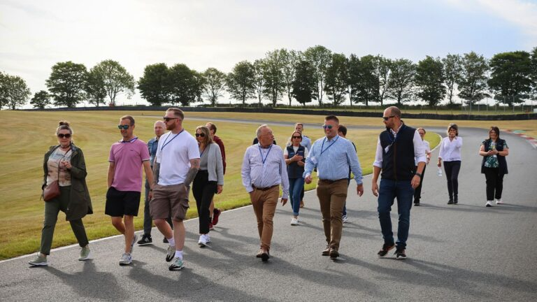 Group of people walking together on a racetrack during the day, surrounded by trees and open fields