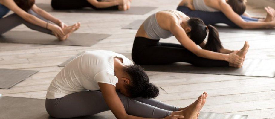 Group yoga class practising seated forward bend pose on mats