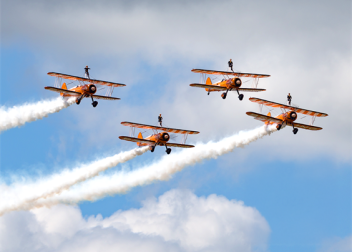 Four vintage biplanes performing an aerial display with wing walkers against a cloudy sky