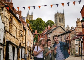 Group of friends exploring historic street in Lincoln, UK with cathedral spires in background, enjoying sightseeing adventure