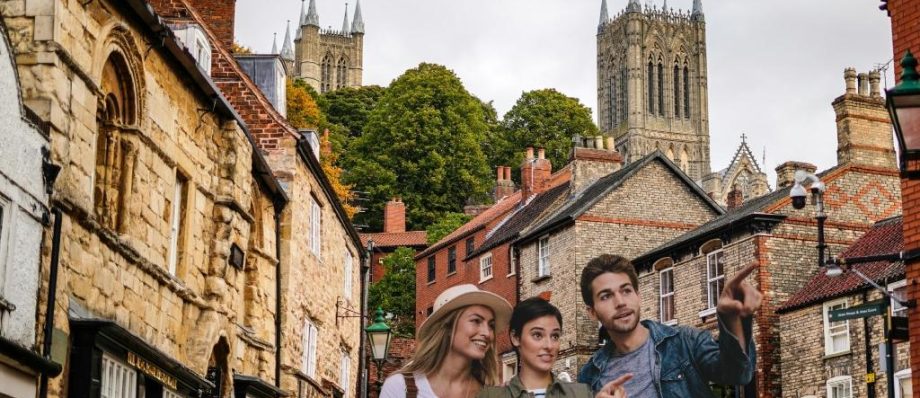 Group of friends exploring historic street in Lincoln, UK with cathedral spires in background, enjoying sightseeing adventure