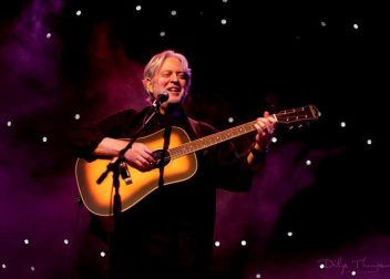 Musician performing live on stage with an acoustic guitar against a starlit backdrop