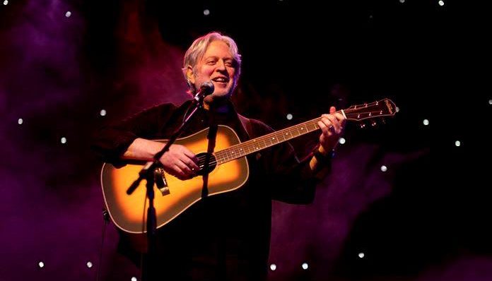Musician performing live on stage with an acoustic guitar against a starlit backdrop