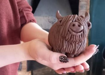 Person holding a handcrafted clay Highland cow sculpture with detailed fur design