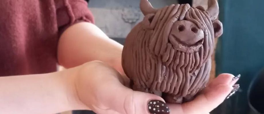 Person holding a handcrafted clay Highland cow sculpture with detailed fur design