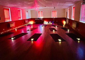 Dimly lit yoga studio with mats laid out, illuminated by soft red and purple lighting ideal for a calming session