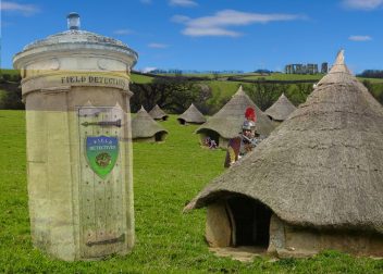 Historic village scene with round thatched huts, Roman soldier, and Field Detectives pillar in scenic countryside