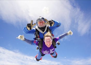 Tandem skydivers mid-air against a clear blue sky, smiling and enjoying the thrill of freefall adventure
