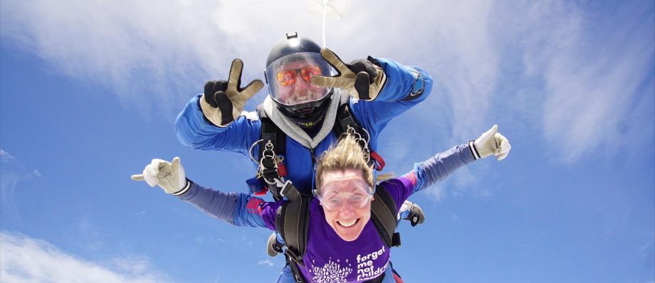 Tandem skydivers mid-air against a clear blue sky, smiling and enjoying the thrill of freefall adventure