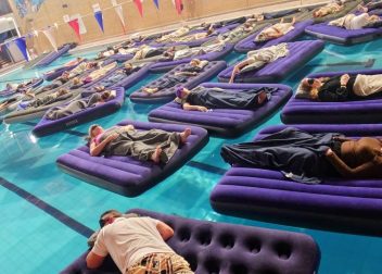People lounging on inflatable mattresses in a swimming pool with colourful mural in the background