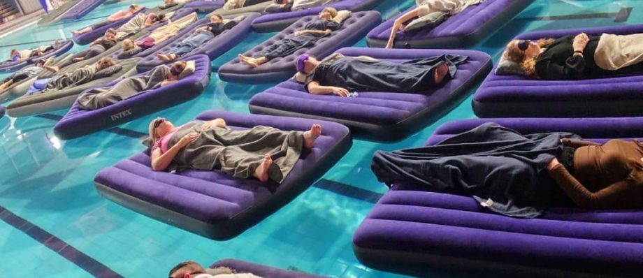 People lounging on inflatable mattresses in a swimming pool with colourful mural in the background