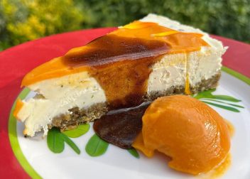 Slice of cheesecake with caramel topping and orange sorbet on a colourful plate outdoors