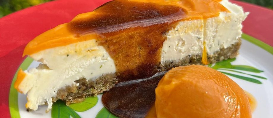 Slice of cheesecake with caramel topping and orange sorbet on a colourful plate outdoors