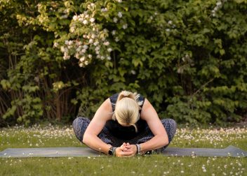 Woman practising yoga outdoors on a mat with greenery and flowers in the background