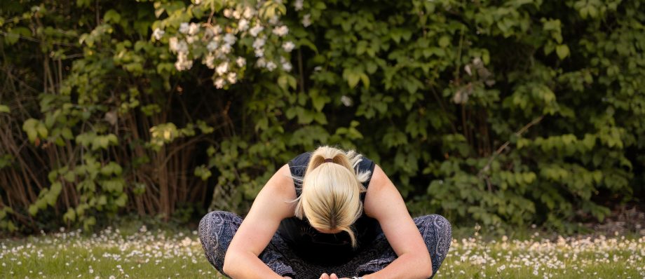 Woman practising yoga outdoors on a mat with greenery and flowers in the background