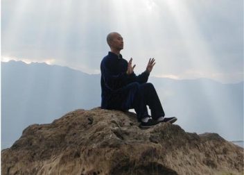 Person meditating on a rock with sun rays and mountains in the background, calm and serene atmosphere