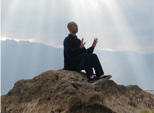 Person meditating on a rock with sun rays and mountains in the background, calm and serene atmosphere