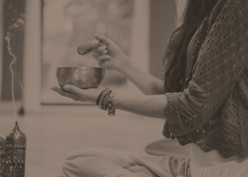 Person using a Tibetan singing bowl in meditation with incense smoke creating a calming atmosphere