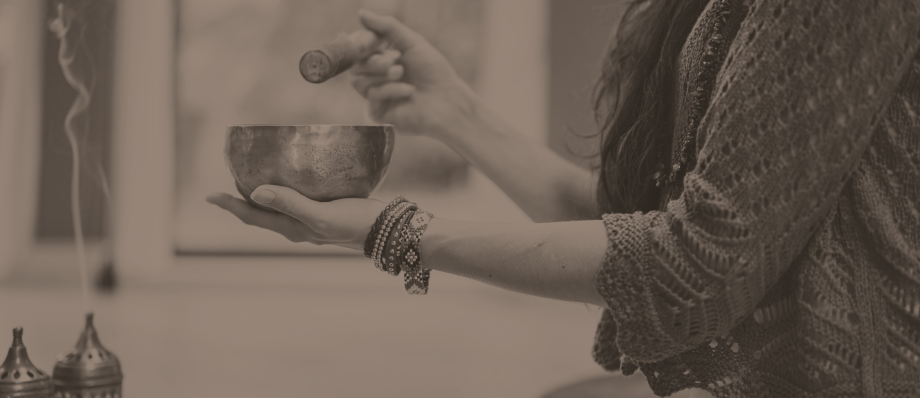 Person using a Tibetan singing bowl in meditation with incense smoke creating a calming atmosphere