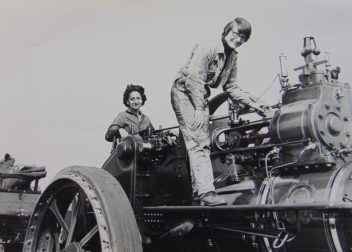Two women operating a vintage steam traction engine in black and white, showcasing historical engineering skills