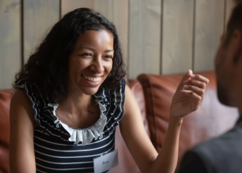 Woman laughing and engaging in conversation with a man on a leather couch in a wooden panelled room