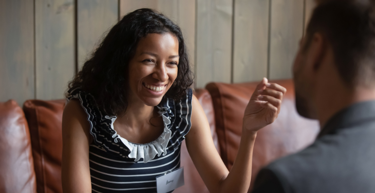 Woman laughing and engaging in conversation with a man on a leather couch in a wooden panelled room