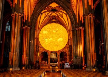 Stunning illuminated sun art installation inside a cathedral with ornate arches and wooden seating rows