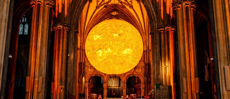 Stunning illuminated sun art installation inside a cathedral with ornate arches and wooden seating rows