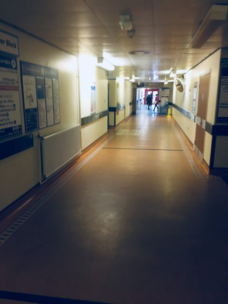 Hospital corridor with signage on the walls and people walking in the distance, creating a sense of depth and movement