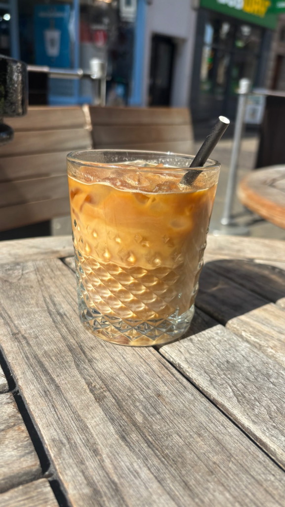 Iced coffee in a textured glass with a straw on a wooden café table, enjoying a sunny day outdoors