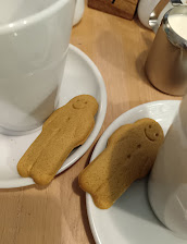 Gingerbread biscuits with smiling faces next to white cups on a wooden table in a cosy setting