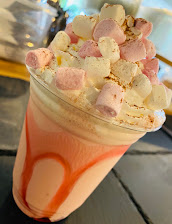 Creamy milkshake topped with pink and white marshmallows in a clear cup, set on a textured grey surface
