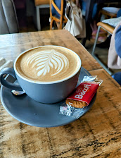 Latte art coffee in grey cup with biscuit on wooden table in cosy café setting
