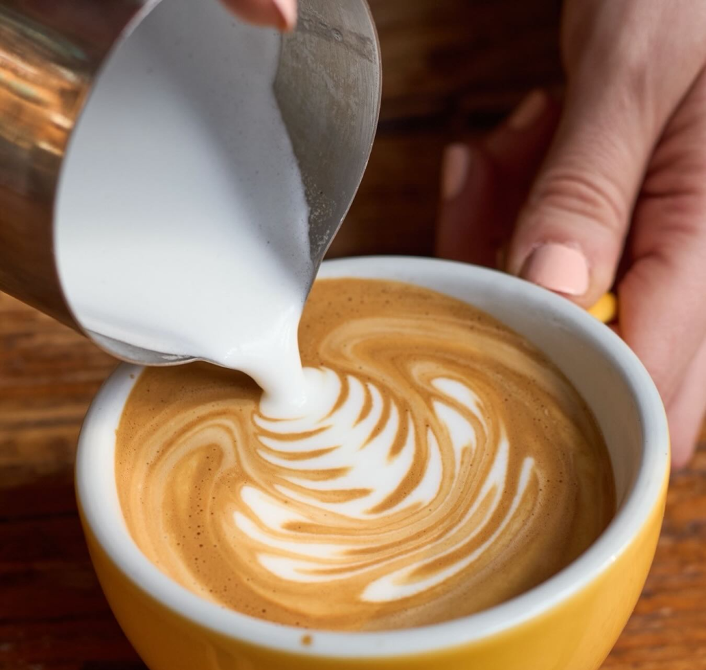 Barista creating intricate latte art in a yellow cup with steamed milk pouring gently over espresso