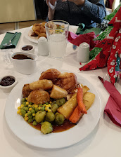 Plate of traditional British roast dinner with vegetables, Yorkshire pudding, gravy, and Christmas decorations in background