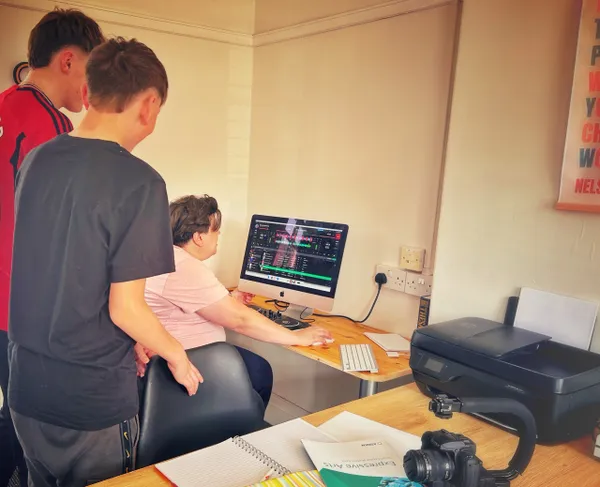 Three people analysing stock market data on a computer in a home office setting with a printer and camera nearby