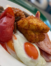 Full English breakfast with eggs, bacon, hash browns, beans, mushrooms, and tomatoes on a white plate