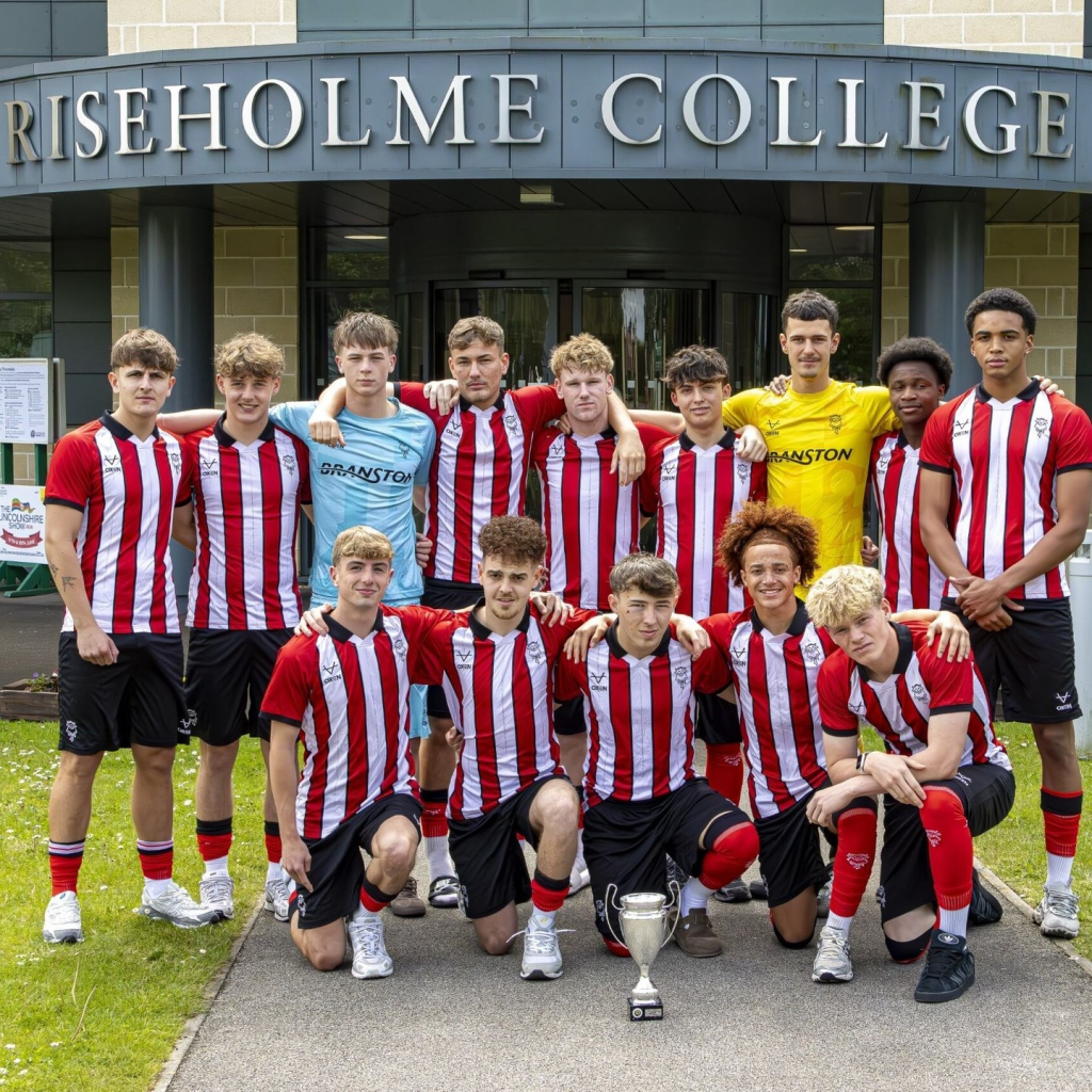Riseholme College football team posing with a trophy outside the college entrance in red and white striped kits