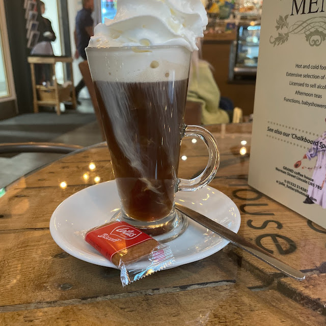 Irish coffee with whipped cream served in a glass mug with a biscuit on a cafe table in a cosy setting
