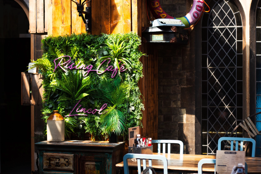 Cosy café with neon sign and lush greenery, featuring a rustic setting with vintage decor and natural sunlight
