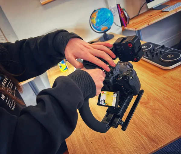Person using a gimbal-mounted camera for filming indoors, with a globe and DJ equipment in the background