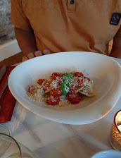 A person holding a bowl of ravioli with cherry tomatoes and grated cheese in an elegant restaurant setting