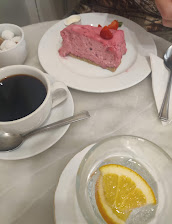 Pink mousse cake with strawberries, black coffee, sugar cubes, and lemon water on a marble table setting