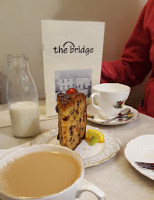 Afternoon tea with fruitcake, milk bottle and teacup at The Bridge café, with person in red jacket in the background