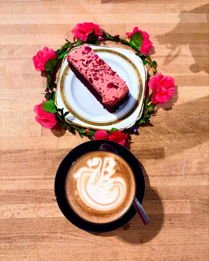 Latte art cappuccino with a raspberry chocolate cake on a flower-adorned plate on a wooden table