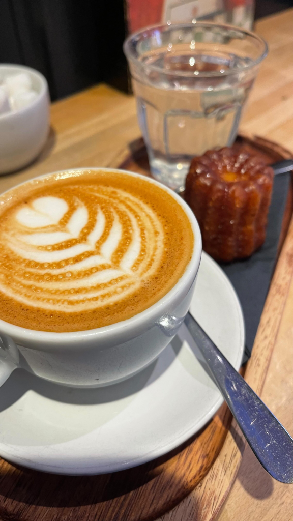 Cup of latte with art, a glass of water, and a pastry on a wooden table in a cosy café setting